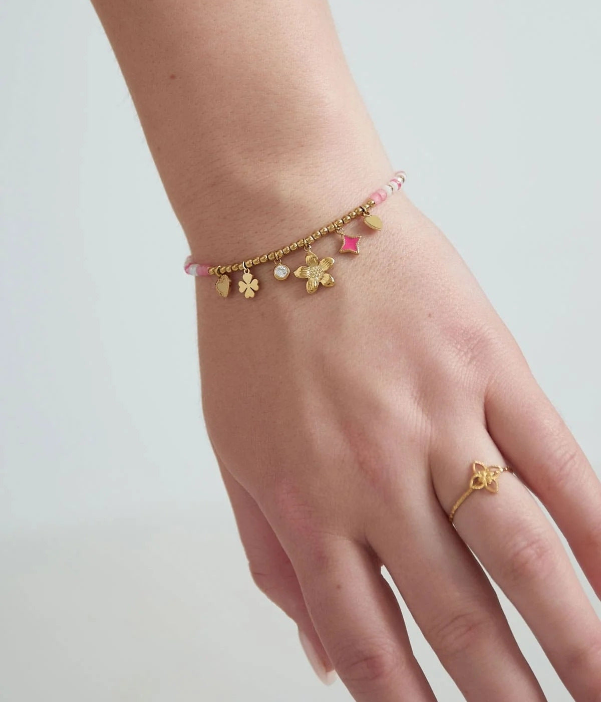 goldenes Armband mit rosafarbenen Steinen und Anhängern in verschiedenen Formen, präsenteiert an einer weiblichen Hand