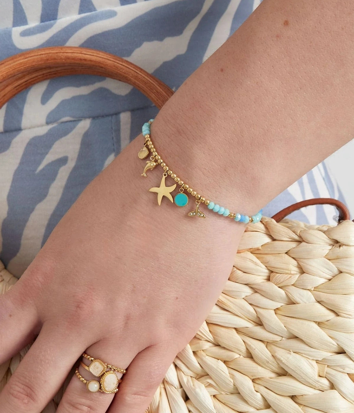 goldenes Armband mit blauen Steinen und Anhängern in verschiedenen Formen, präsenteiert an einer weiblichen Hand