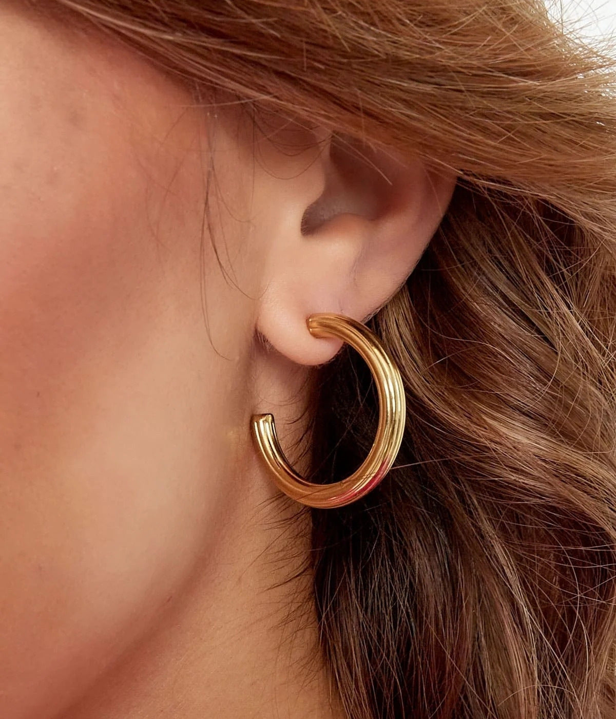 Nahaufnahme von goldenen Ohrringen nicht ganz rund, getragen von einer Frau