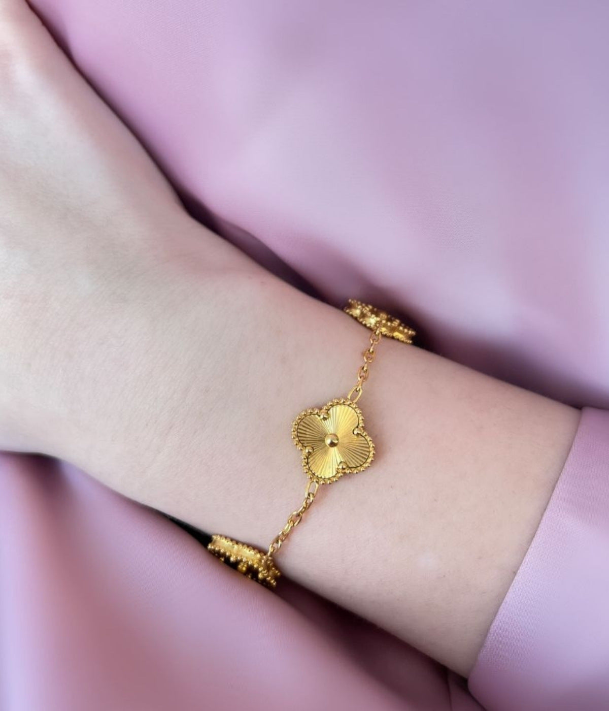 Goldenes Armband an einer Frauen Hand angezogen. Das Armband hat goldene vierblättrige Kleeblätter
