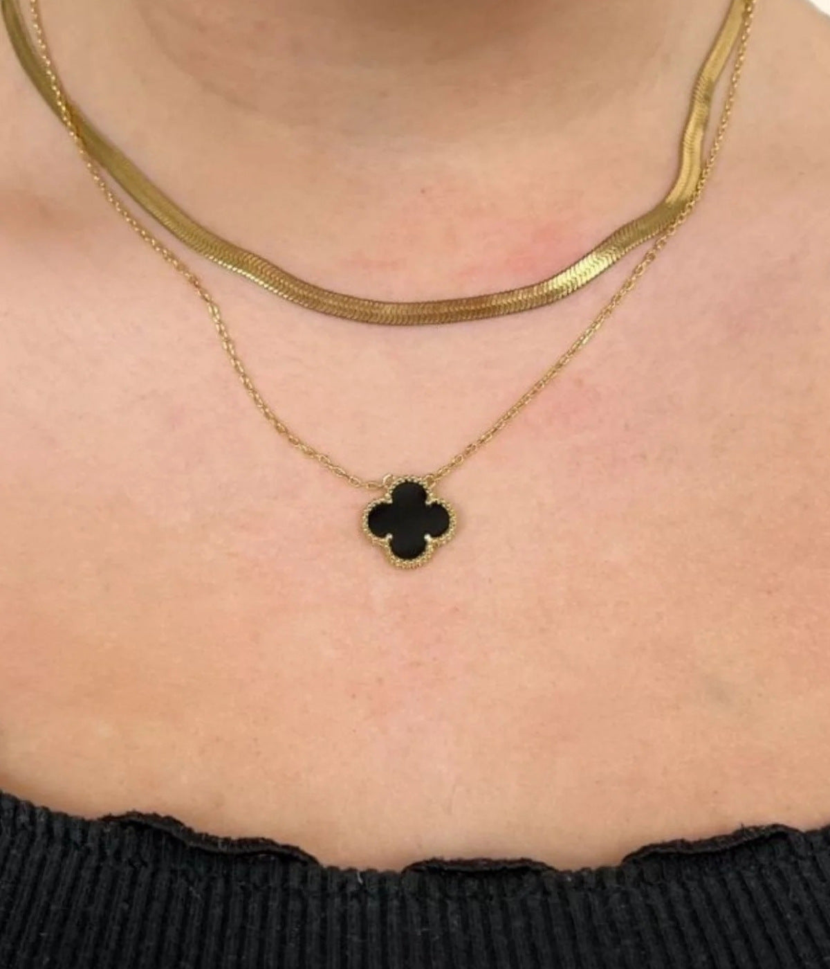 Frau die zwei Ketten trägt. Eine goldene Choker Kette und eine goldene Kette mit schwarzem Kleeblatt Anhänger