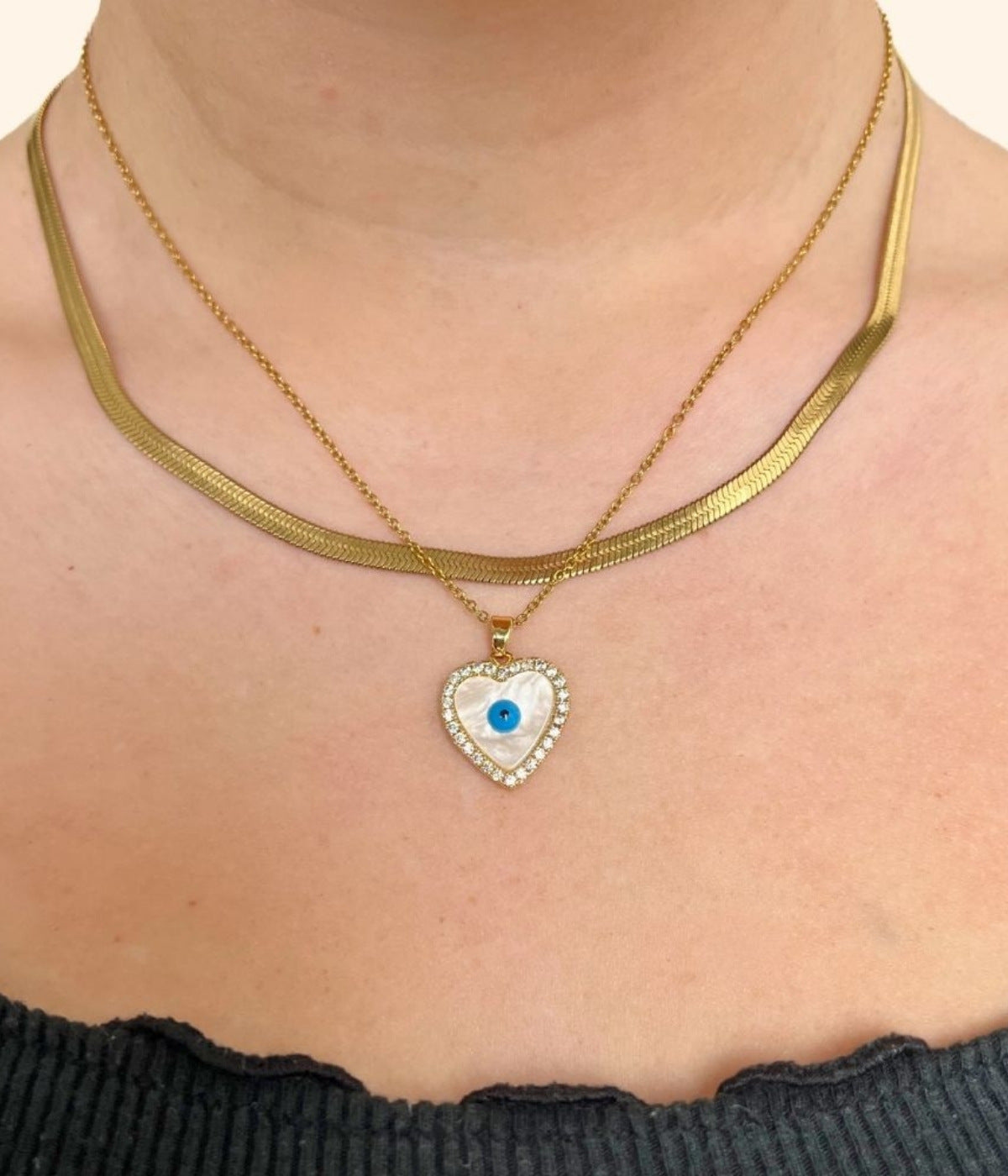 goldene Choker Kette mit einer Kette mit weißem Herz Anhänger kombiniert, mit einem blauen Auge in der Mitte, getragen von einer Frau