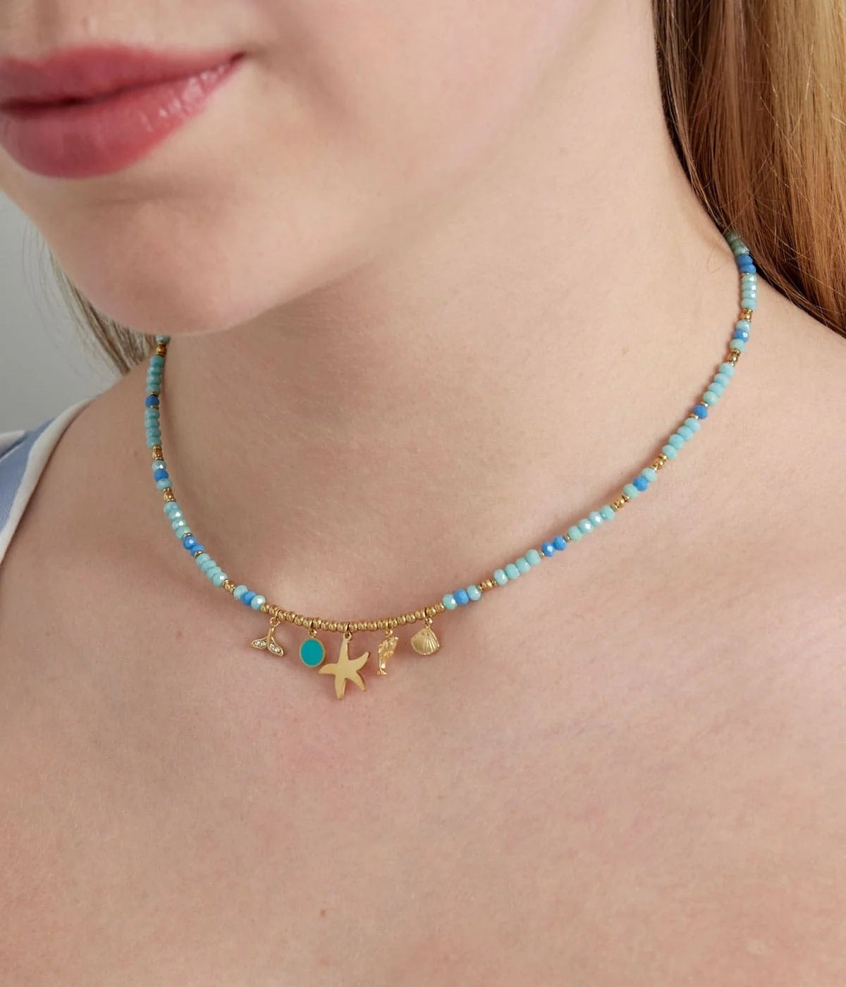goldene Kette mit blauen Steinen und goldenen Anhängern in unterschiedlichen Farben, getragen von einer Frau