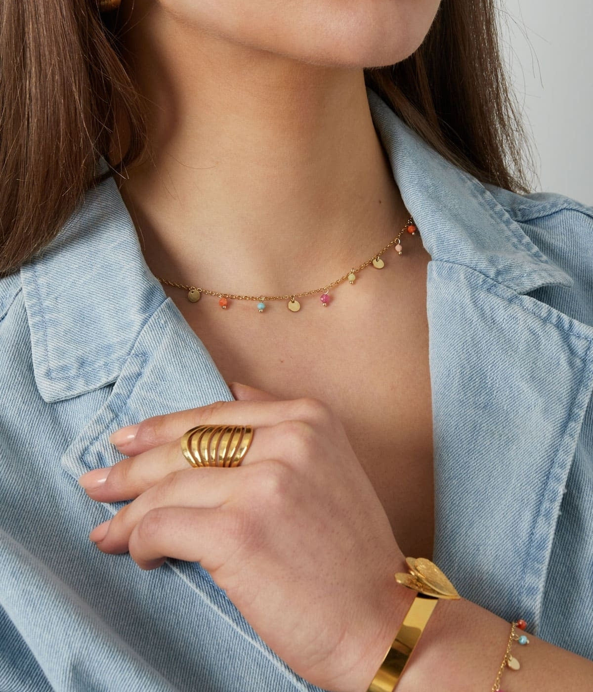 Nahaufnahme von einer goldene Kette und Armband mit Anhängern bestehend aus bunten steinen und goldenen Plättchen, angezogen an einer Frau