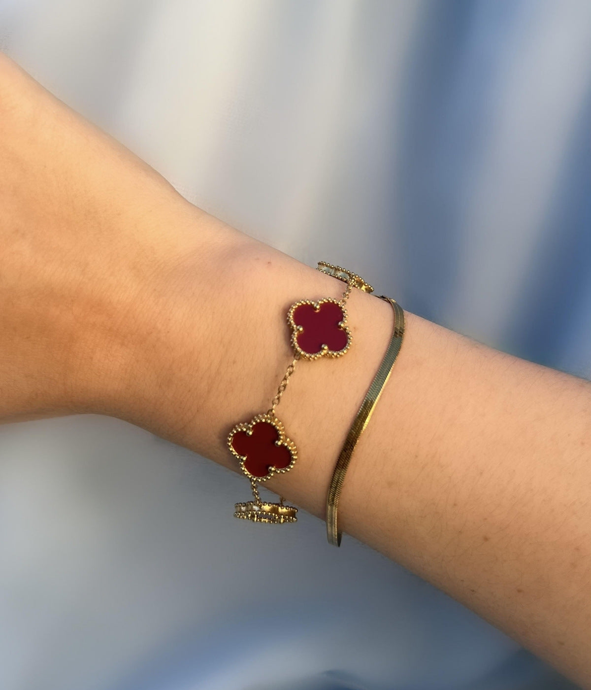 Weinrotes Kleeblatt Armband aus Gold am Handgelenk getragen – stilvoller Glücksbringer Schmuck