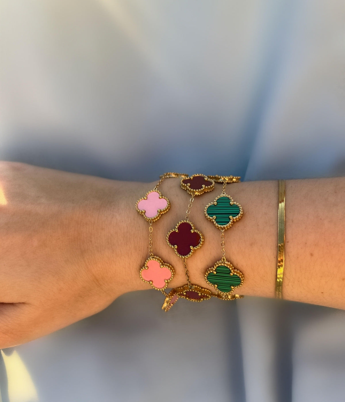 Kombination mehrerer Kleeblatt Armbänder in Rosa, Rot und Grün – trendiger Goldschmuck getragen