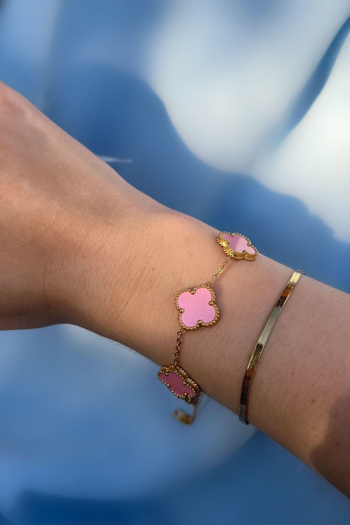 Zartes rosa Kleeblatt Armband aus Gold am Handgelenk getragen – femininer Schmuck mit Symbolcharakter