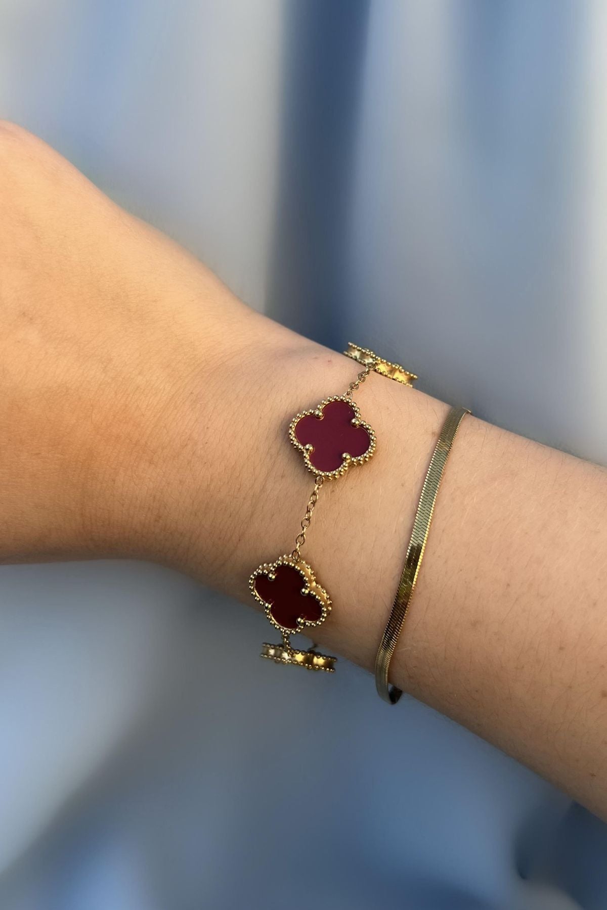Weinrotes Kleeblatt Armband aus Gold am Handgelenk getragen – stilvoller Glücksbringer Schmuck