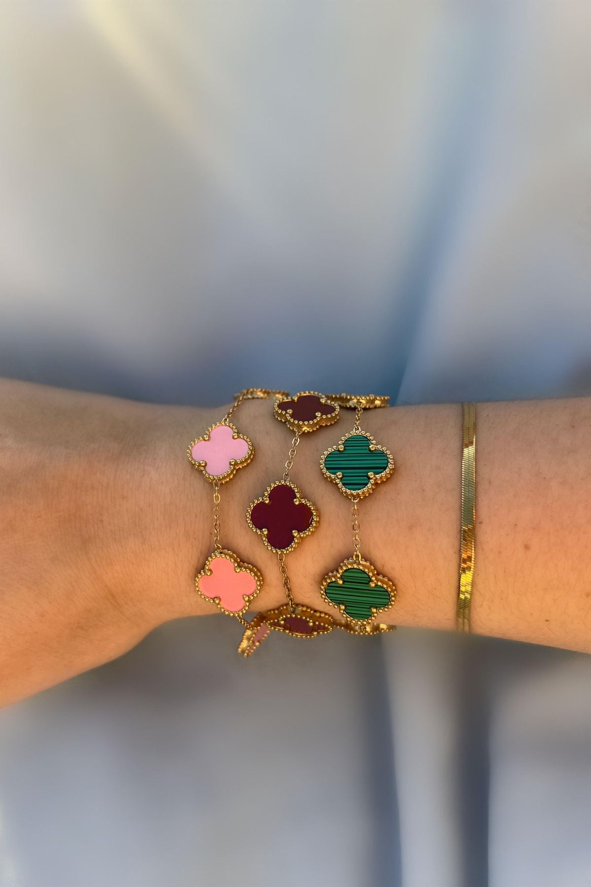 Kombination mehrerer Kleeblatt Armbänder in Rosa, Rot und Grün – trendiger Goldschmuck getragen