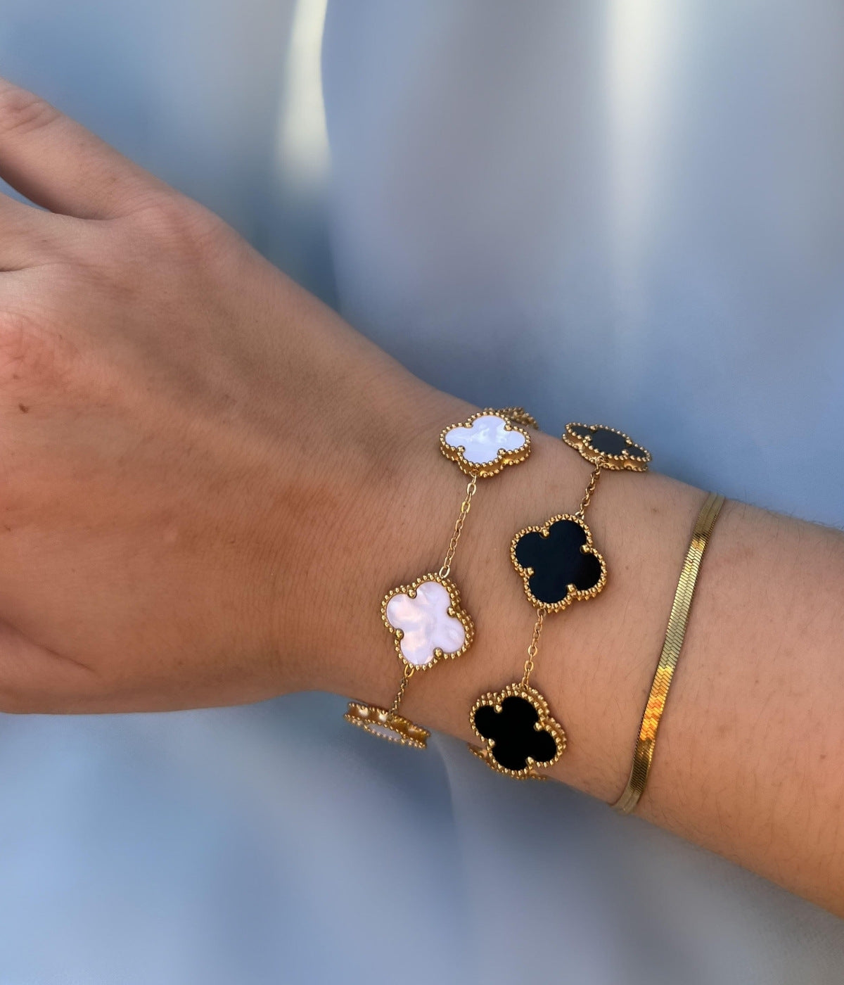 Elegante Armbänder in Schwarz und Perlmutt mit vierblättrigem Kleeblatt Design – luxuriöses Damenarmband getragen an einem Frauen Unterarm